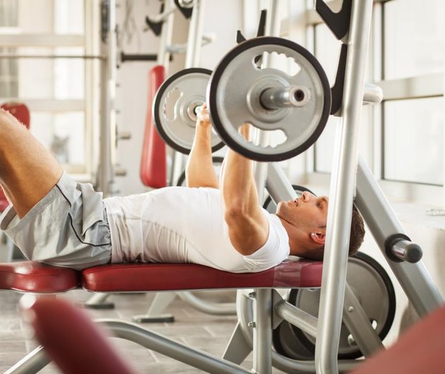 Muscular man lies on a bench and performs heavy weights presses at the fitness center.