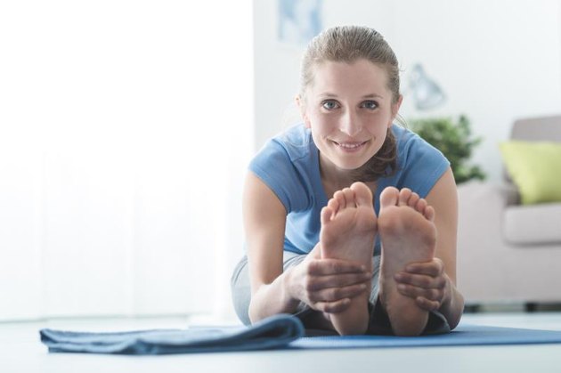 Woman practicing yoga and meditation at home on the floor, she is bending and holding her feet