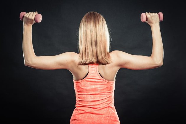 Bodybuilding. Strong fit woman exercising with dumbbells. Muscular blonde girl lifting weights back view studio shot on black background