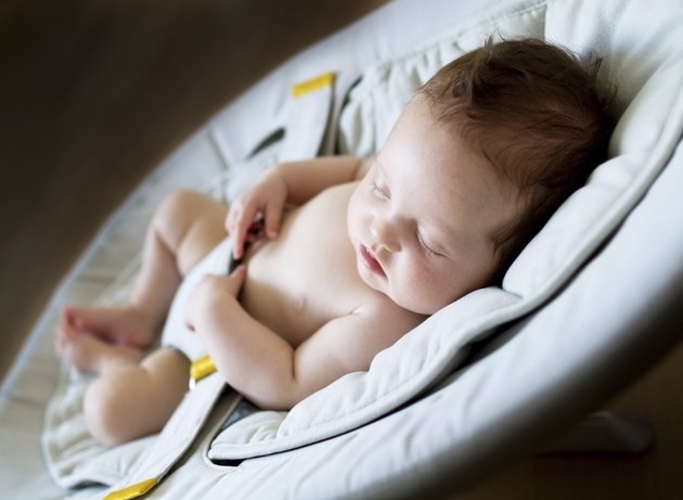 Newborn baby girl sleeping on bouncer chair in dark room