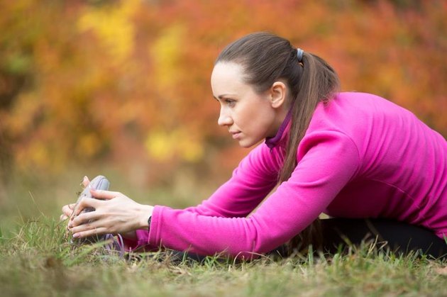 Sporty beautiful young woman practicing yoga, doing seated Hamstring Stretch, forward bend pose, paschimothanasana, stretching before running routine, working out outdoors on autumn day. Side view