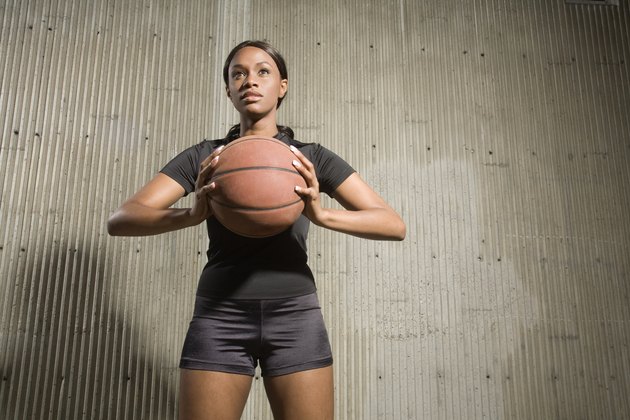 Portrait of young woman holding a basketball, photographed from a low perspective