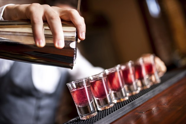 close-up of barman hand pouring alcohol into shot glasses