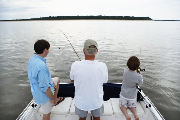 Senior man with son and grandson (10-11) fishing from boat, rear view