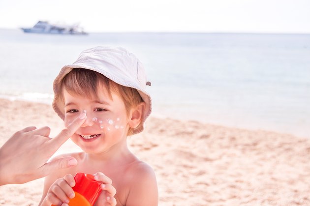 Hand of mother applying suncream to her son on beach.