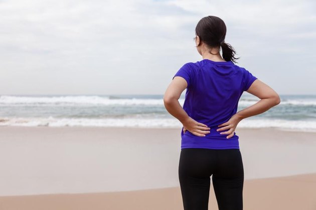 Female athlete suffering from a back injury at the beach on an Autumn day.