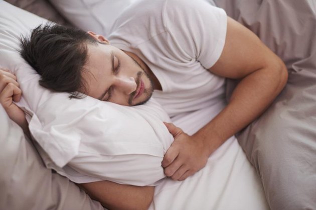 A tired man rests in the bed.