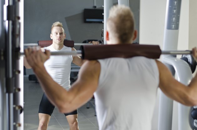 Handsome young man doing squats in gym