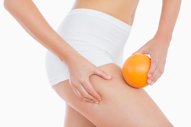 Woman squeezing fat on thigh as she holds orange