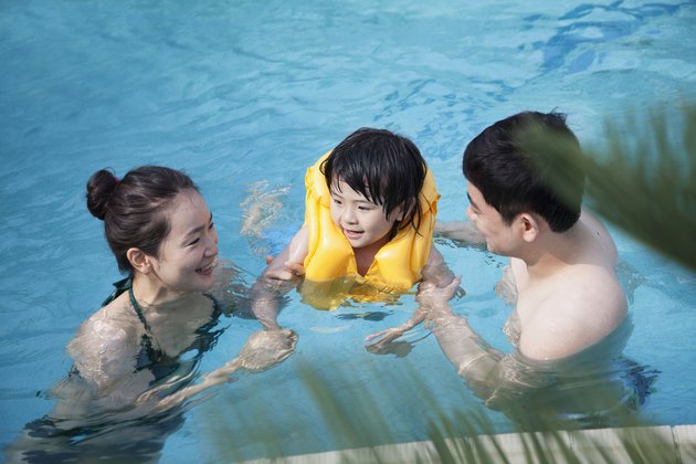 Happy smiling family teaching son how to swim in the pool
