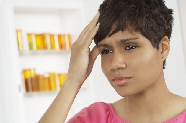 Woman with hand on head, near pill cabinet
