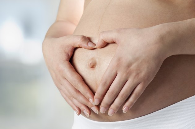 Young pregnant woman making heart shape on belly, close up