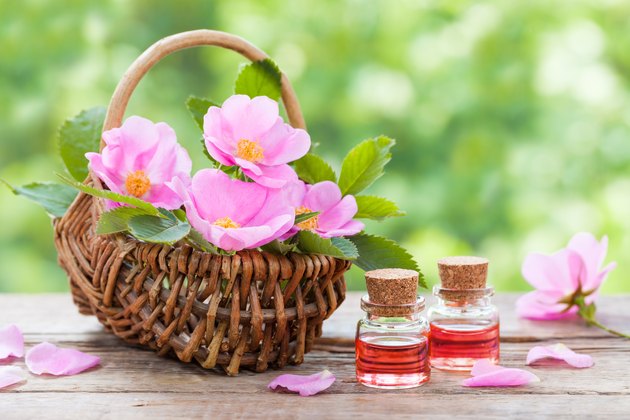 Basket with pink rose hip flowers and bottles of oil