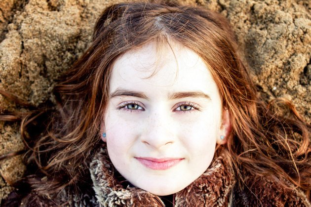 Head shot portrait of young girl lying back on beach