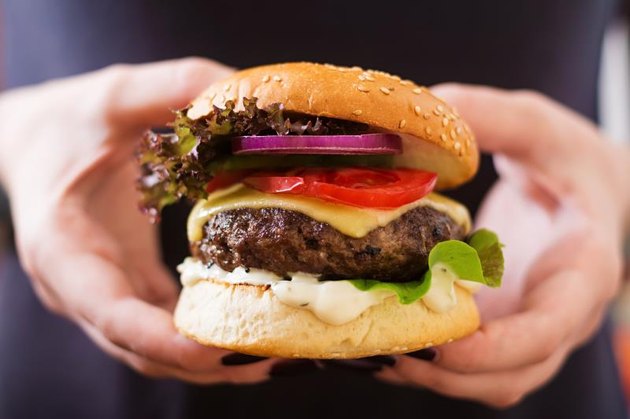 Big sandwich - hamburger burger with beef, cheese, tomato and tartar sauce in female hands