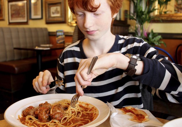 Image of boy eating spaghetti meatballs pasta in Italian restaurant