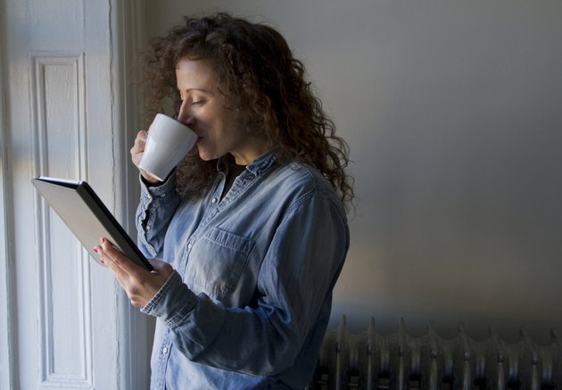 Traveller Stood At Window With Coffee Reading iPad