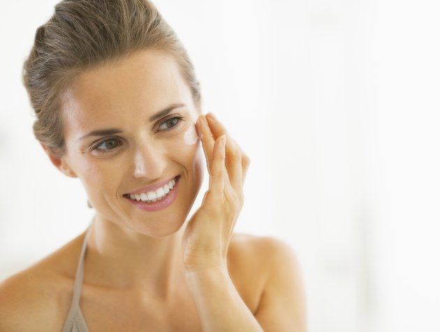 portrait of happy young woman applying cream in bathroom