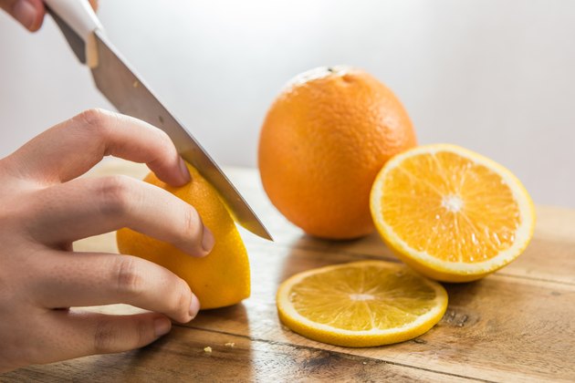 Hand slicing orange on wooden board