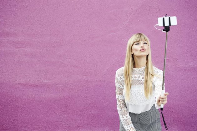 Blond beautiful blogger kissing for selfie against pink background