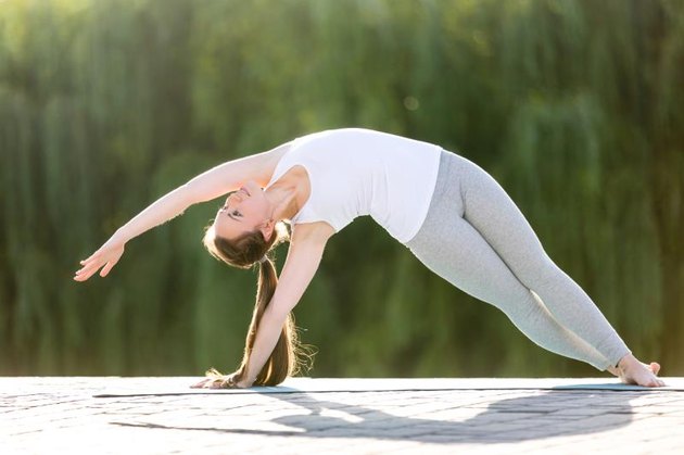 Sporty beautiful young woman practicing yoga, standing in Bending Side Plank exercise, vasistasana pose, working out, wearing sportswear, outdoor full length, summer park background