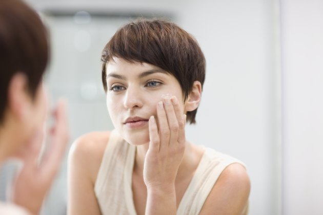 Woman applying moisturizer in mirror