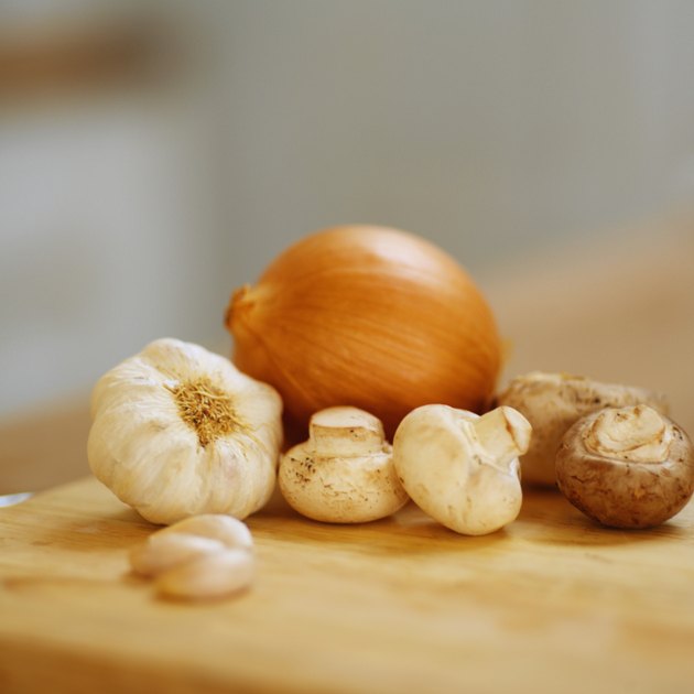 Close up of an onion and clove garlic and mushrooms lying on a chopping board
