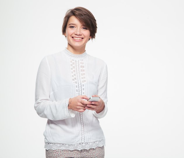 Cheerful cute lovely young woman holding and using cell phone