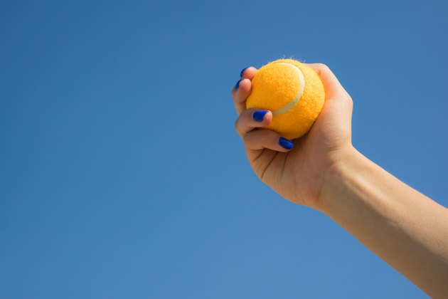 Female hand holds a bright orange tennis ball