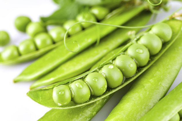 Pods of green peas with drops on white background