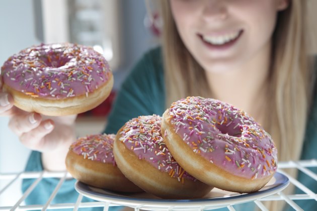 woman taking pink doughnut out of fridge