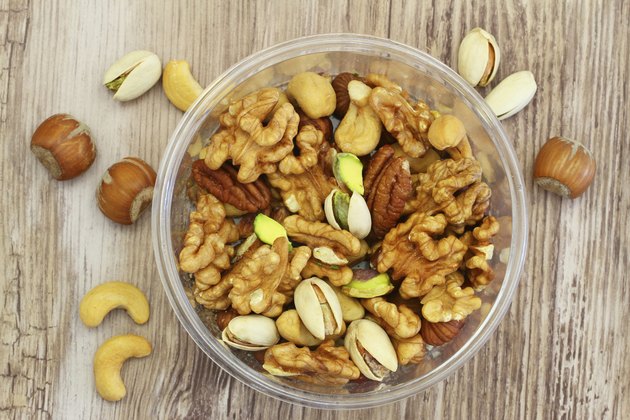 Selection of mixed nuts in plastic box on wooden surface