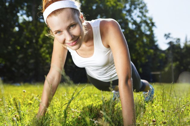 Young woman doing push ups on green grass.