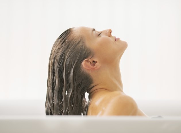 young woman washing hair in bathtub