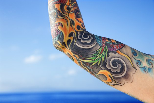 Close up of tattooed woman' || chr(39) || 's arm with Pacific Ocean in background in Maui, Hawaii, USA.