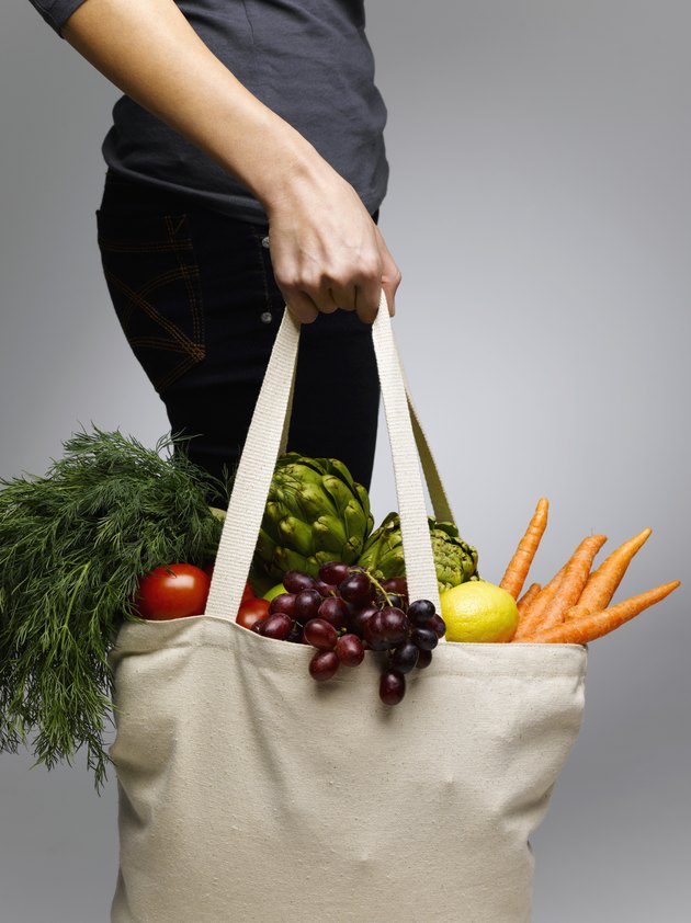 Woman holding grocery bags containing vegetables, mid section