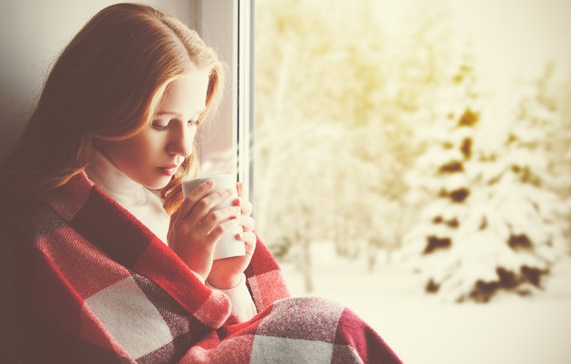 Pensive sad girl with a warming drink looking ou window