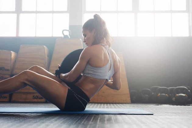 Woman doing sit ups with holding a weight plate. Fitness woman working out on core muscles at gym gym.