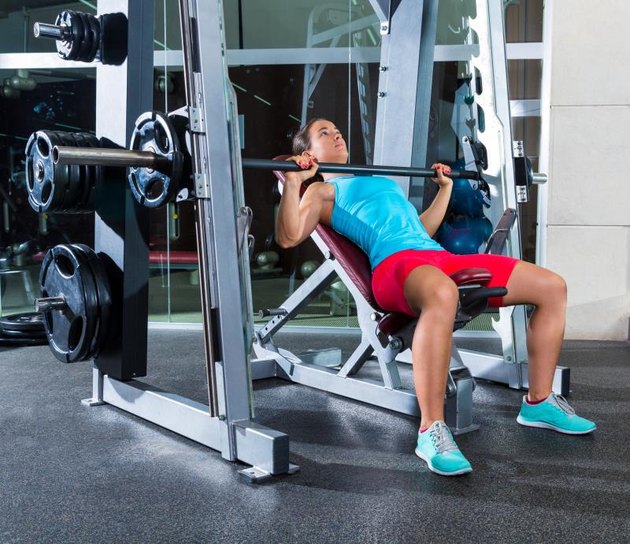 Barbell Incline Bench Press woman in multipower Smith machine workout at gym