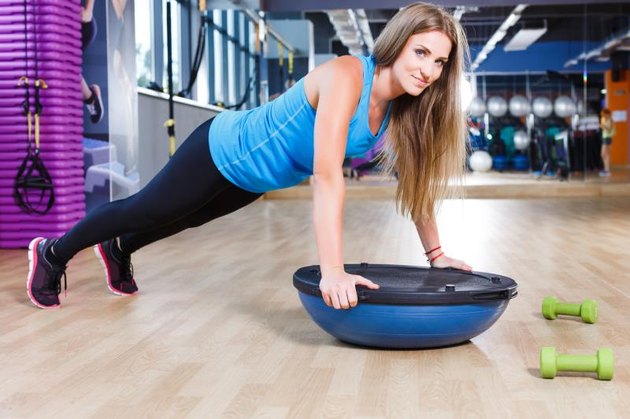 Young brunet athletic woman doing pushups on a bosu ball in the gym