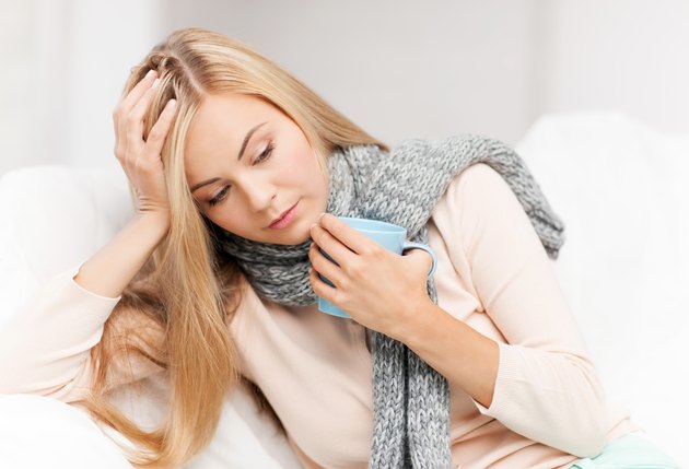Unwell blonde woman wearing a scarf, holding head and a mug