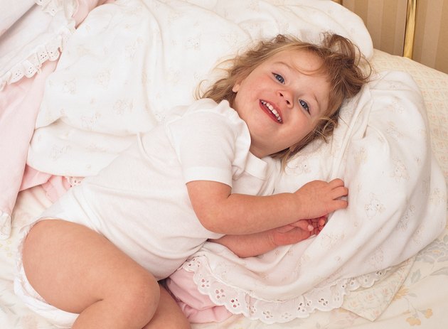 a young redheaded girl lays in bed as she smiles and snuggles up to a blanket