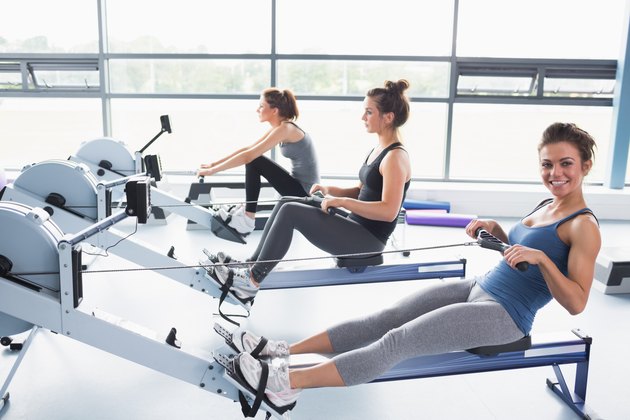 Happy woman using rowing machine with friends