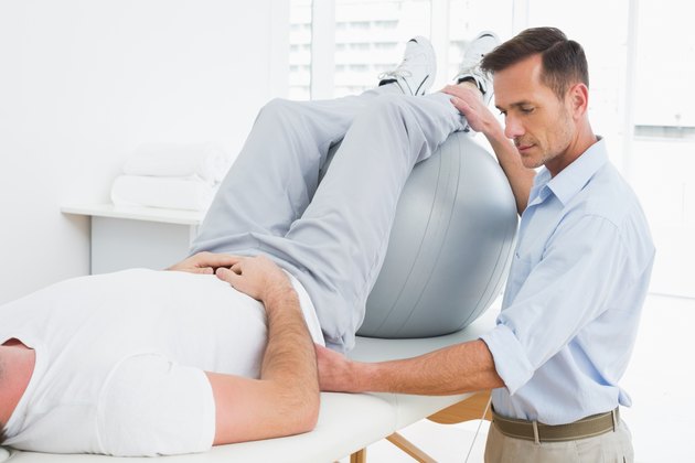 Physical therapist assisting man with yoga ball