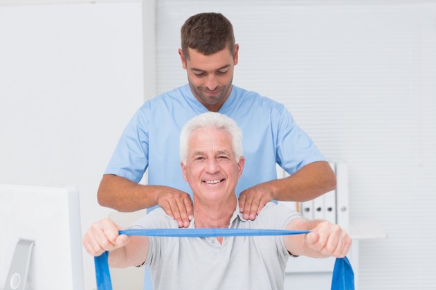 Physiotherapist assisting senior patient in exercising with resistance band