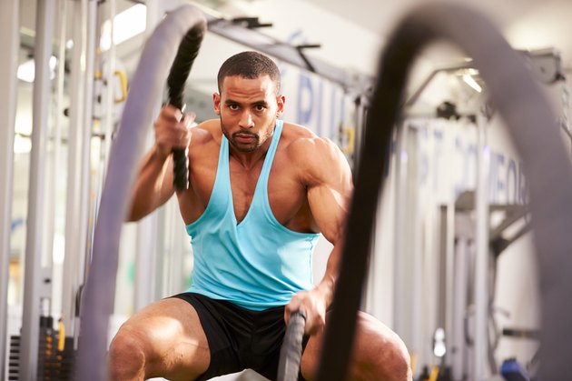 Young man working out with battle ropes at a gym