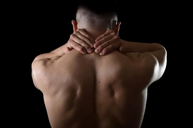 back of young muscular sport man holding sore neck with his hands and touching or massaging cervical area suffering body pain in spine back health problem isolated on black background