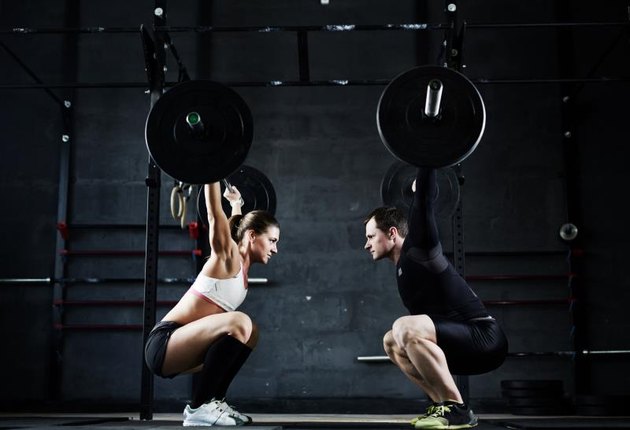 Active young man and woman lifting heavy barbells opposite one another