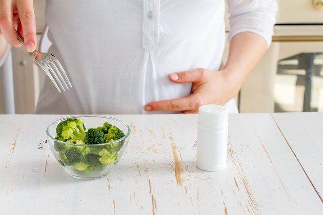 Pregnant female choosing between broccoli in glass bowl and vitamins