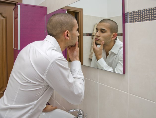 Handsome young man looking at himself in bathroom mirror